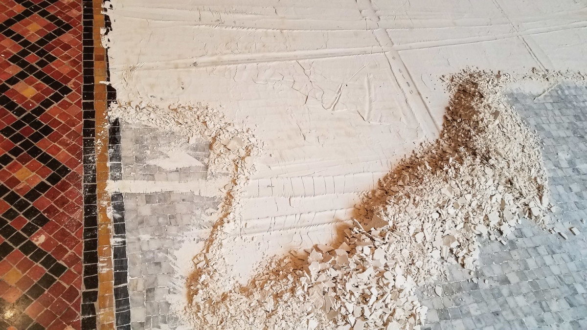 Mosaic stone tile floor with poultice partially in place. The brown discoloration of the white diatomaceous earth is the removed dust and dirt, which was carried onto the floor by a roof leak. To the left is dried poultice partially removed from grey tile. To the right is exposed tile that was already rinsed. 