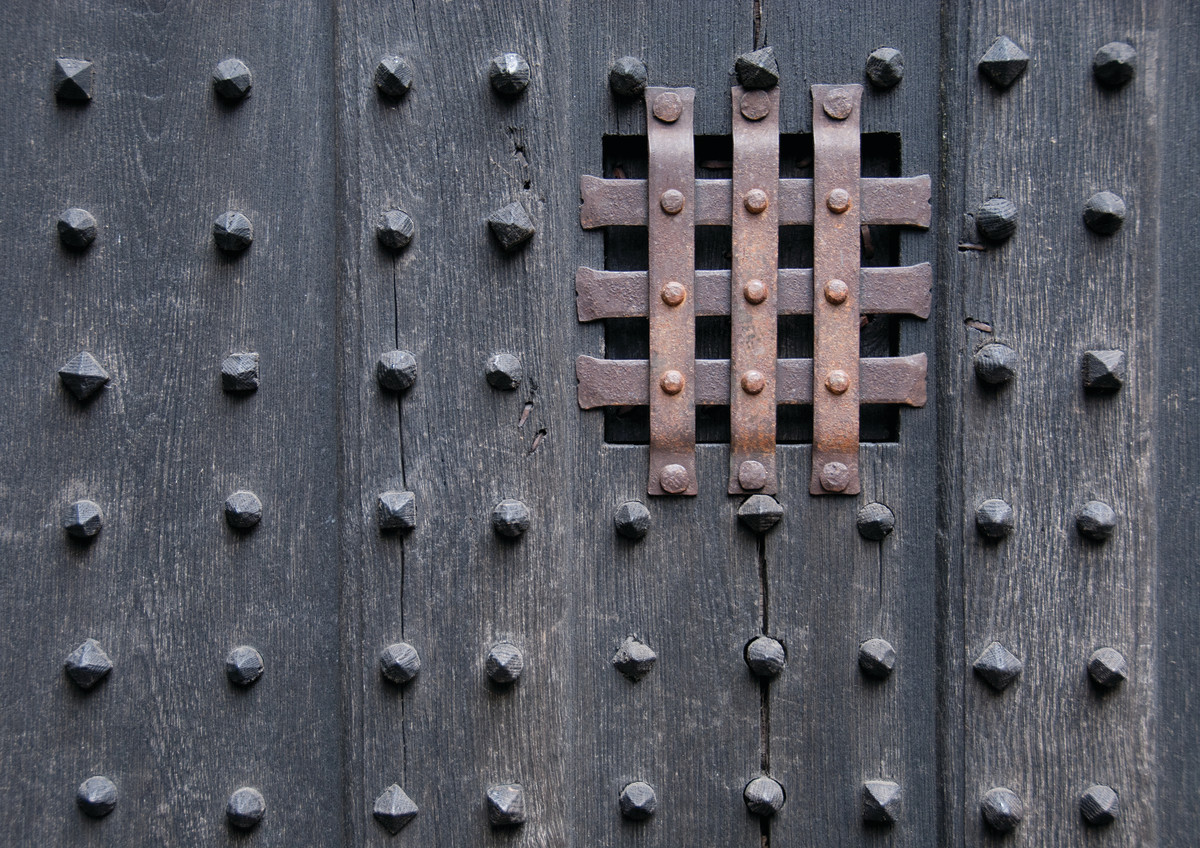 A medieval door with a peephole covered in metal bars.