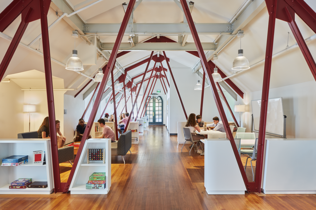 By removing partitions, installing dormer windows, and painting the support trusses bright red, the renovated mezzanine morphed from a cramped former staff quarters to a lively student activity space.