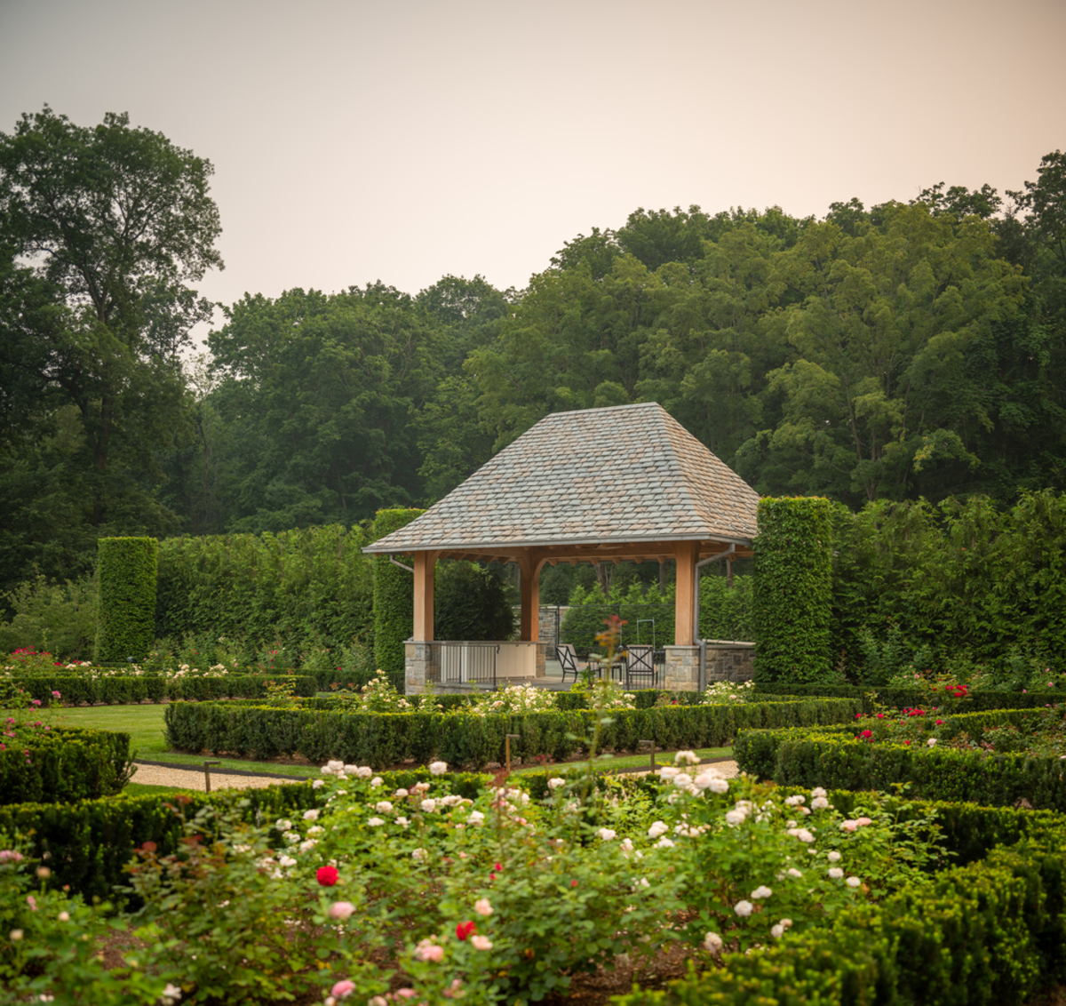 At Rose Manor, whose grounds were designed by Janice Parker Architects, the formal rose garden parterres lead the way to the tennis court pavilion, which is ﬂanked by tightly clipped columnar hornbeams.
